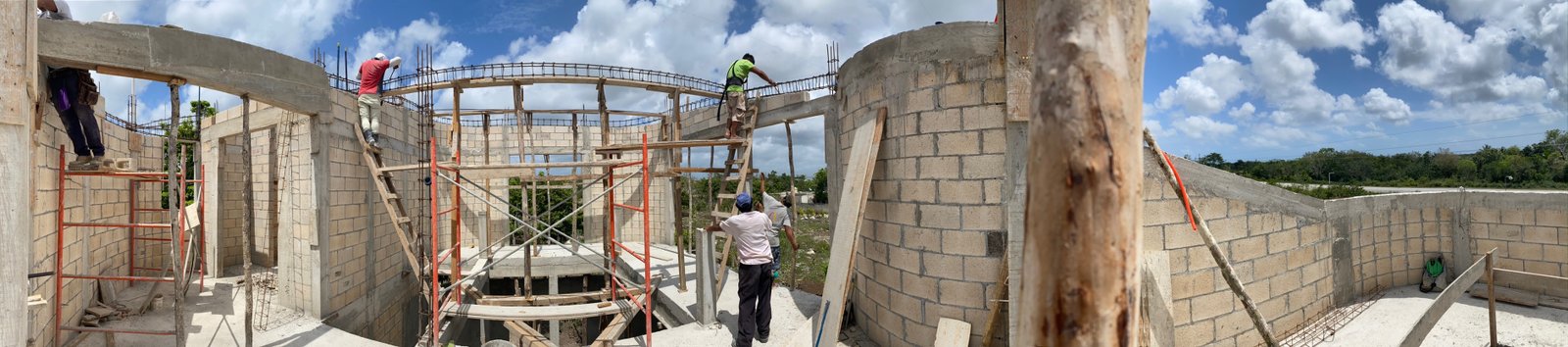 Panorama of the crew raising the Casa Blanca walls, scaffolding and rebar against the sky, Rancho Verde Tulum, Tulum, Mexico