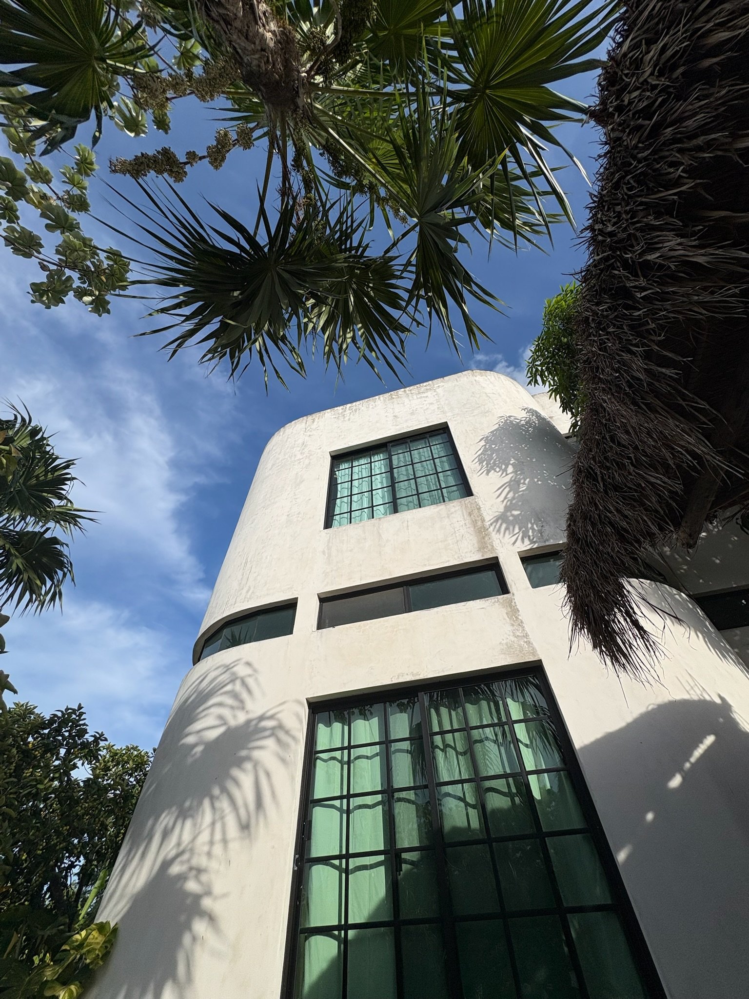 Casa Blanca curved white exterior seen through palm fronds, Rancho Verde Tulum, Tulum, Mexico