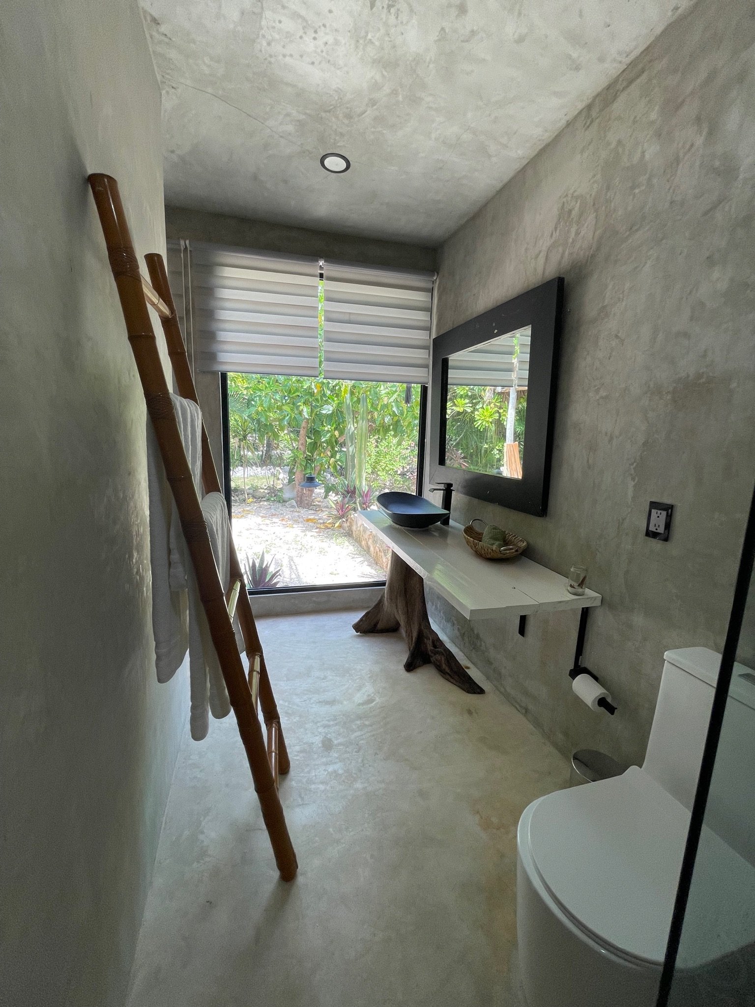 Concrete bathroom with a tree-trunk vanity, bowl sink and bamboo towel ladder, Rancho Verde Tulum, Tulum, Mexico