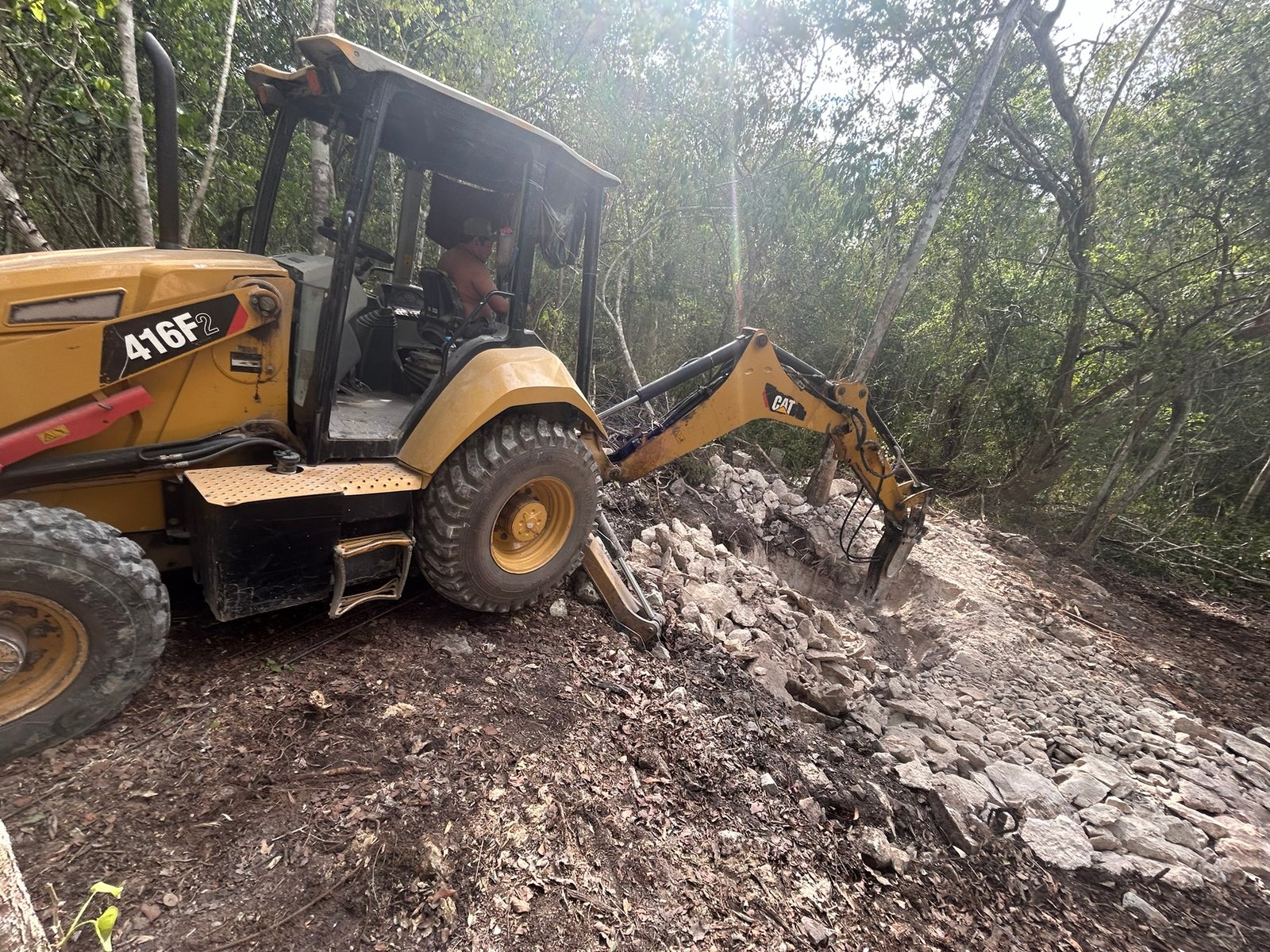 Backhoe breaking through limestone to cut the first access trench in the jungle, the very start of the build, Rancho Verde Tulum, Tulum, Mexico