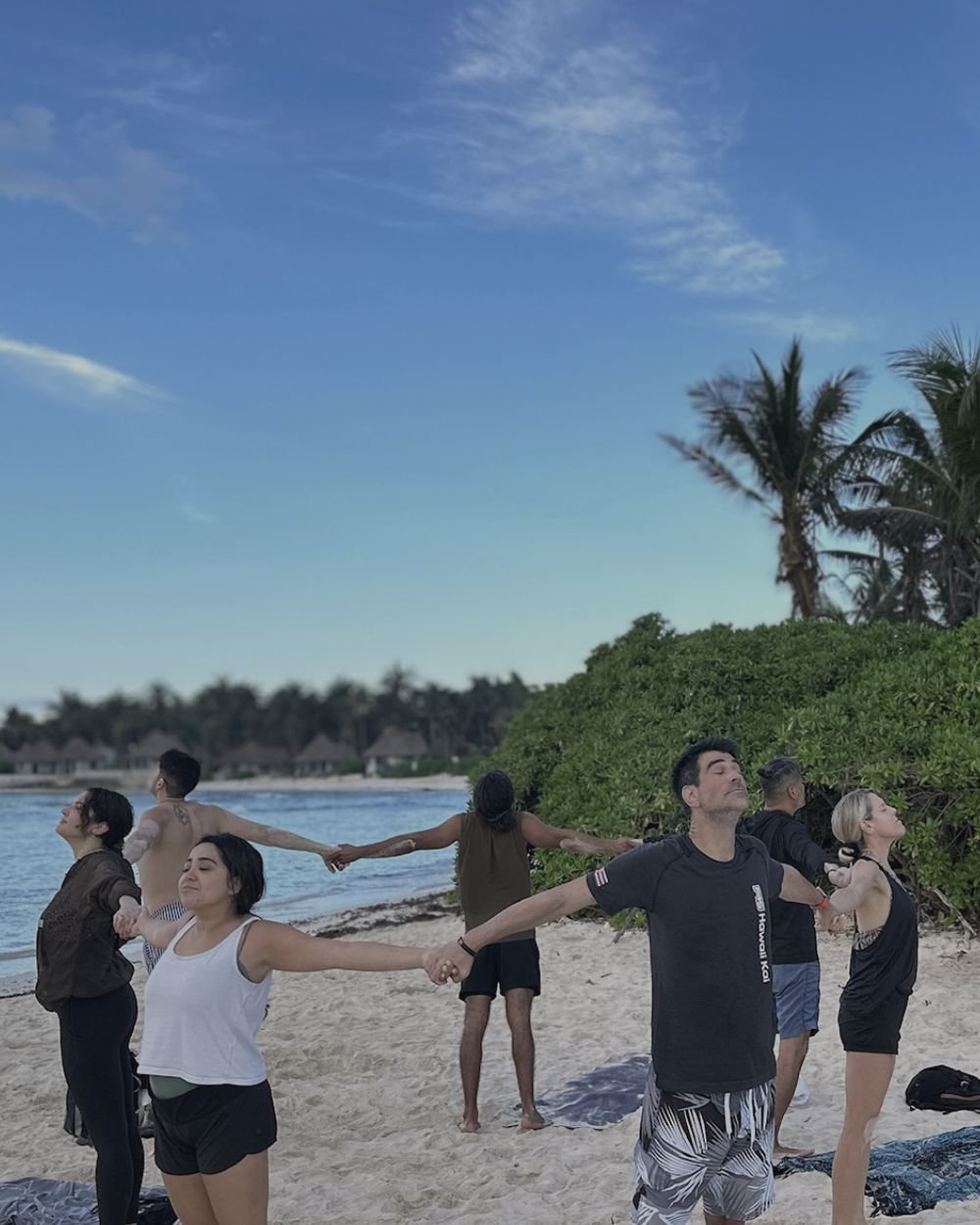 Retreat group holding hands in a circle with eyes closed on a Tulum beach