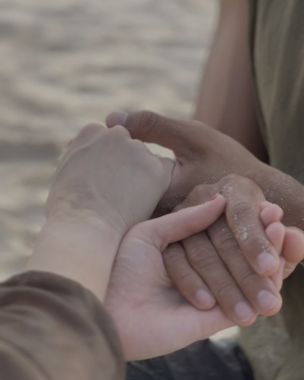 Sandy hands held together during a human connection exercise on the beach near Tulum