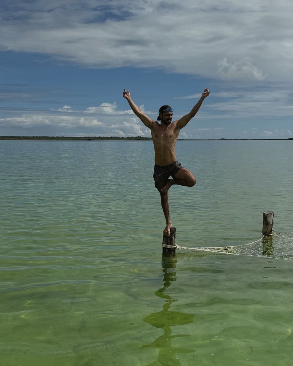 Retreat guest balancing in tree pose on a post in a turquoise lagoon near Tulum