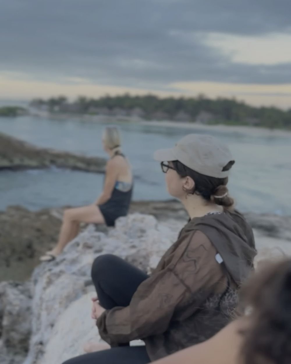 Retreat guests resting on coastal rocks after a gentle climb, looking out over the Caribbean Sea near Tulum