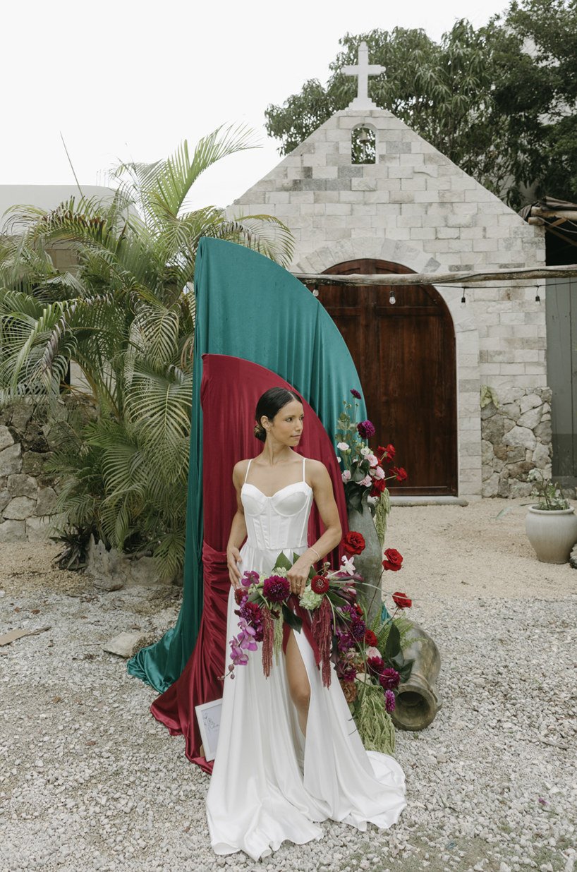 Bride with a burgundy bouquet in front of the arched chapel door at Rancho Verde Tulum
