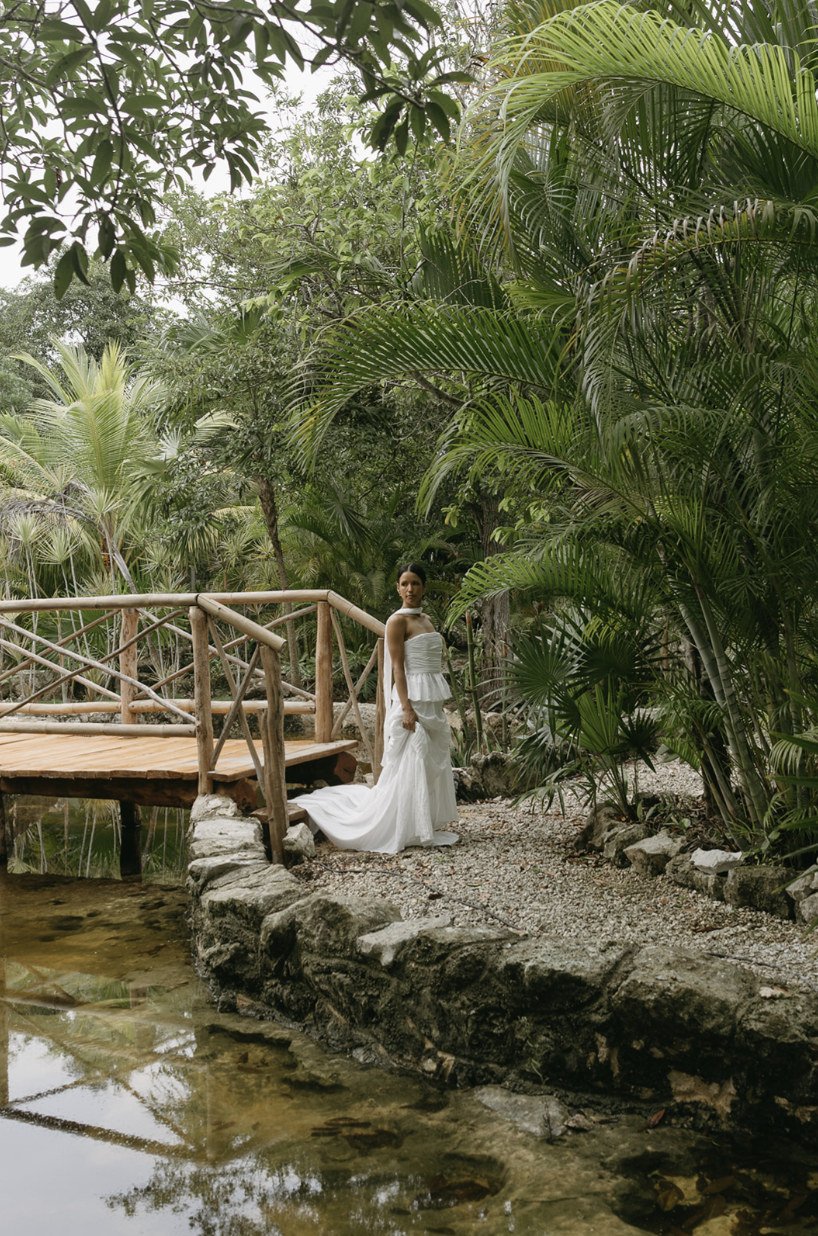 Bride beside the wooden bridge over the pond, framed by palms, at Rancho Verde Tulum