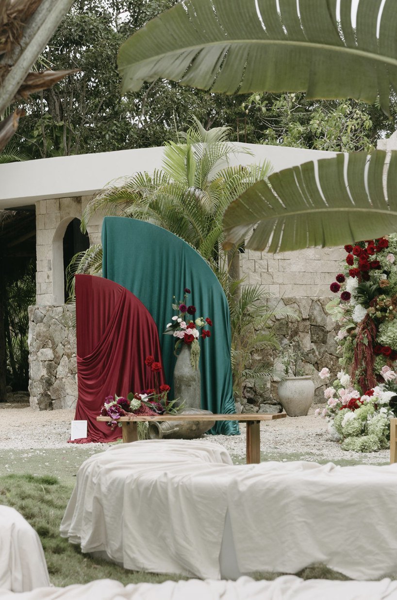 Draped emerald and burgundy ceremony backdrop with florals before the stone chapel at Rancho Verde Tulum