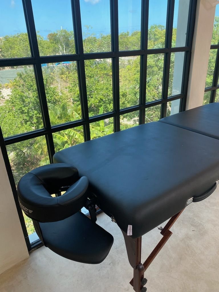 Massage table beside tall black-framed windows overlooking the jungle at Rancho Verde Tulum