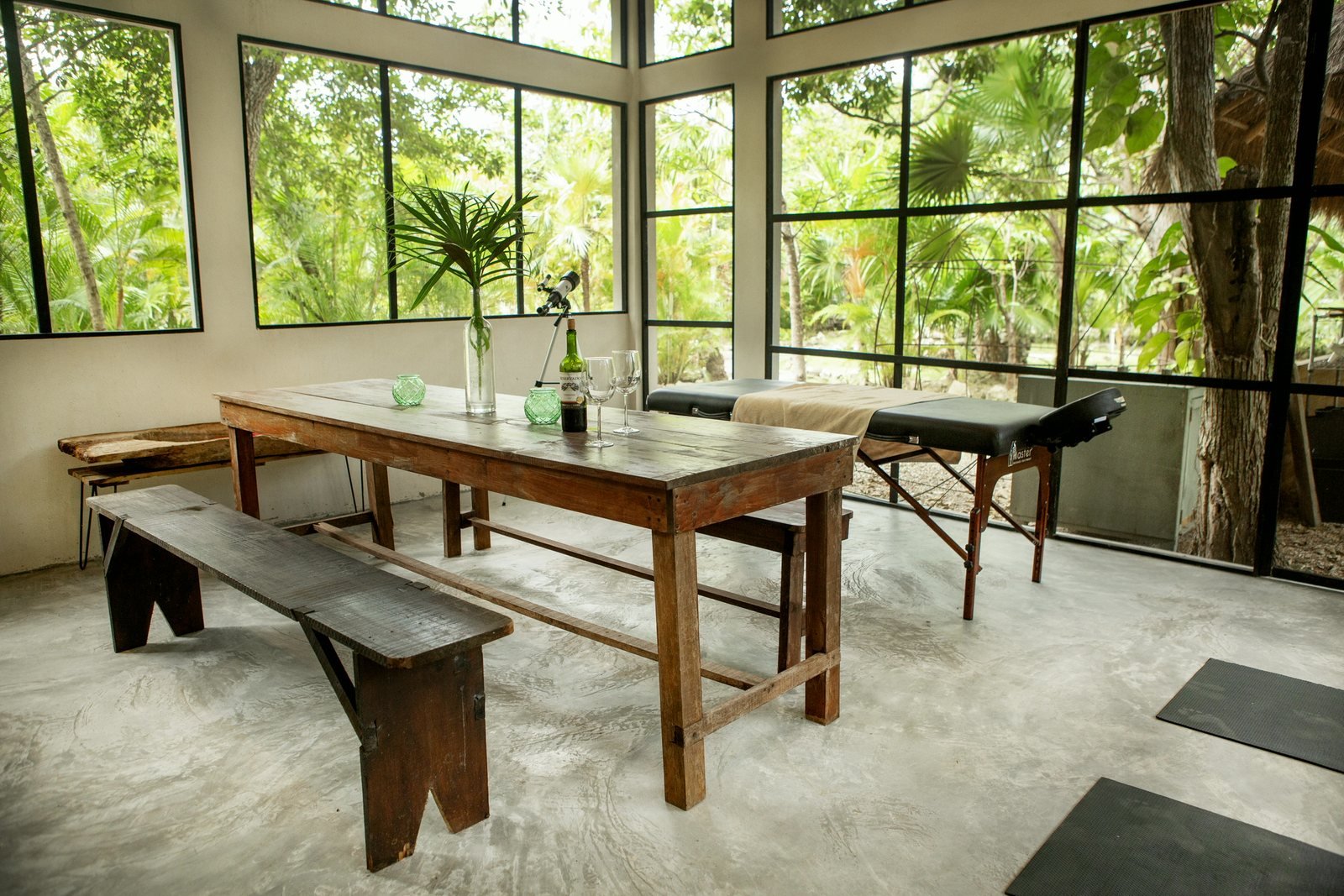Sunroom with a long wooden table, massage table and floor-to-ceiling jungle windows, Rancho Verde Tulum retreat sanctuary, Tulum Mexico