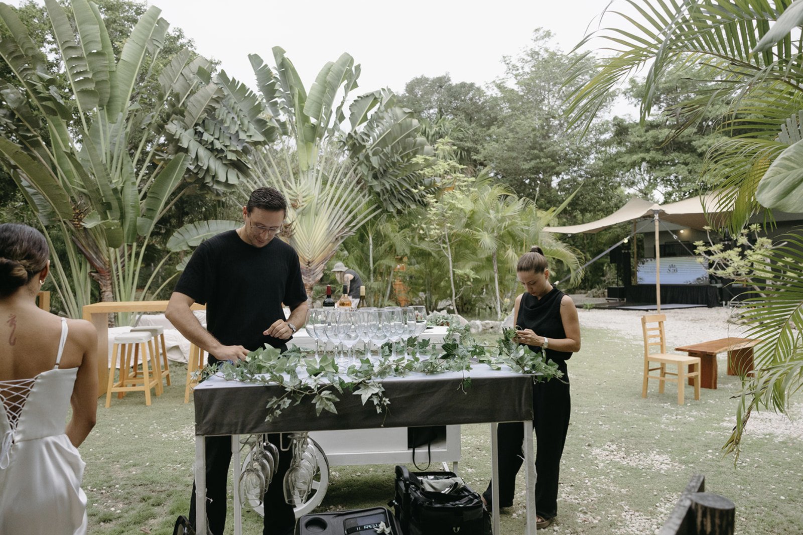 Bartenders dressing a white bar cart with ivy and glassware on the lawn at Rancho Verde Tulum